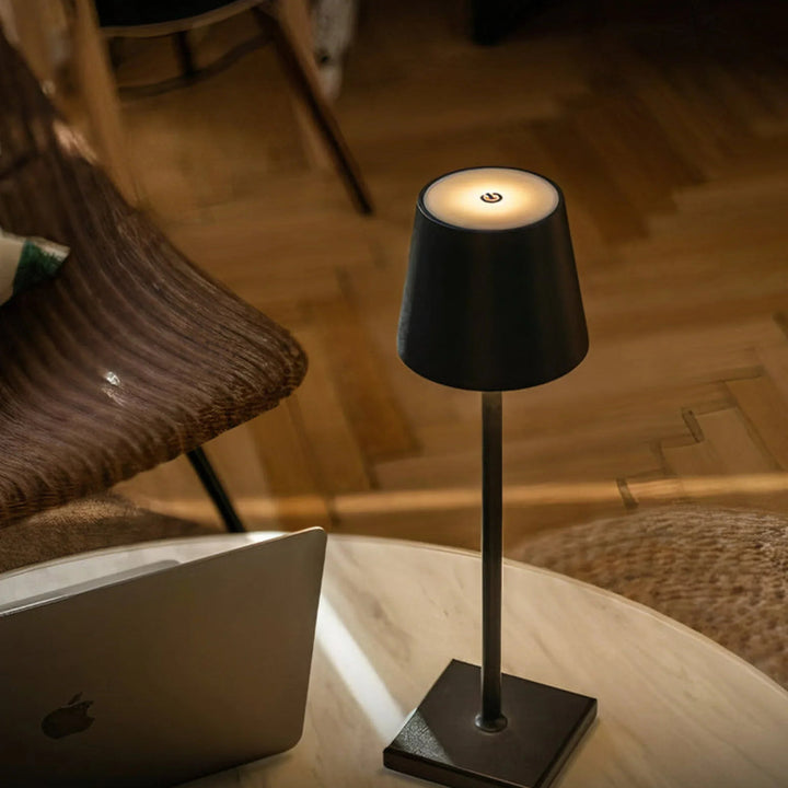 Small black lamp on a table next to a laptop with a wooden chair in the background.